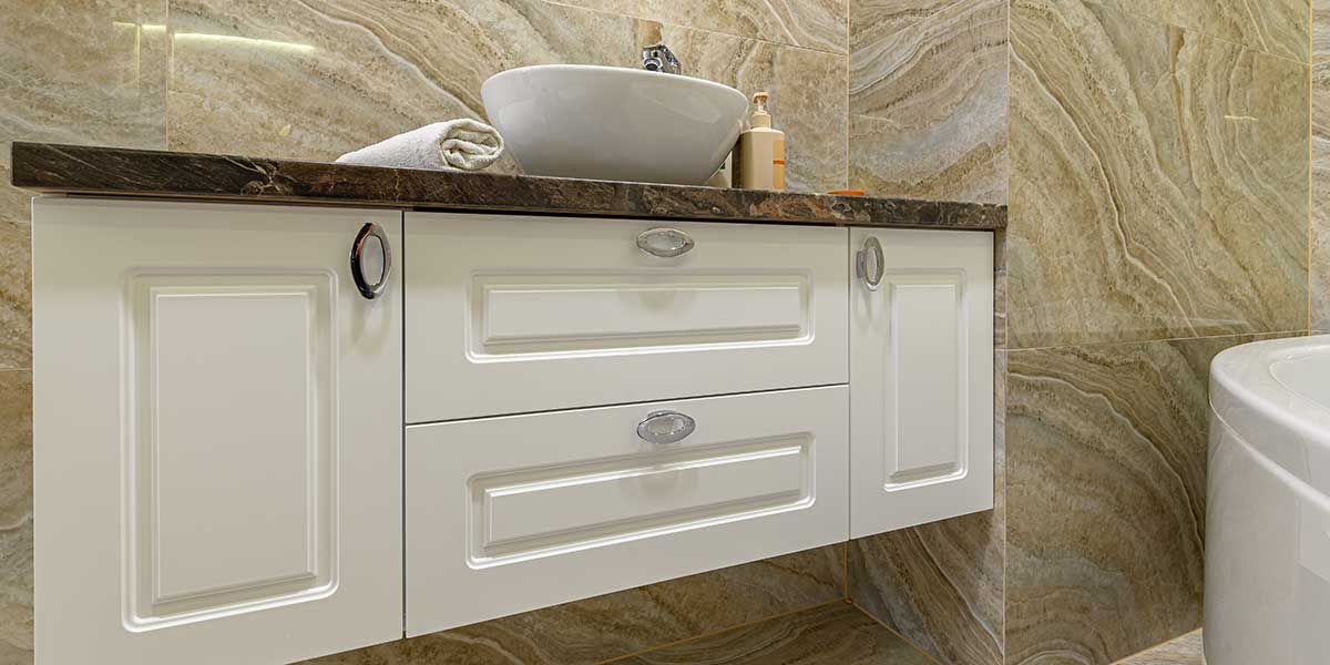 Bathroom Cabinet Hardware Finishes White bathroom vanity with oval silver knobs against marble tiles, showcasing stylish cabinet hardware finishes for modern home design.